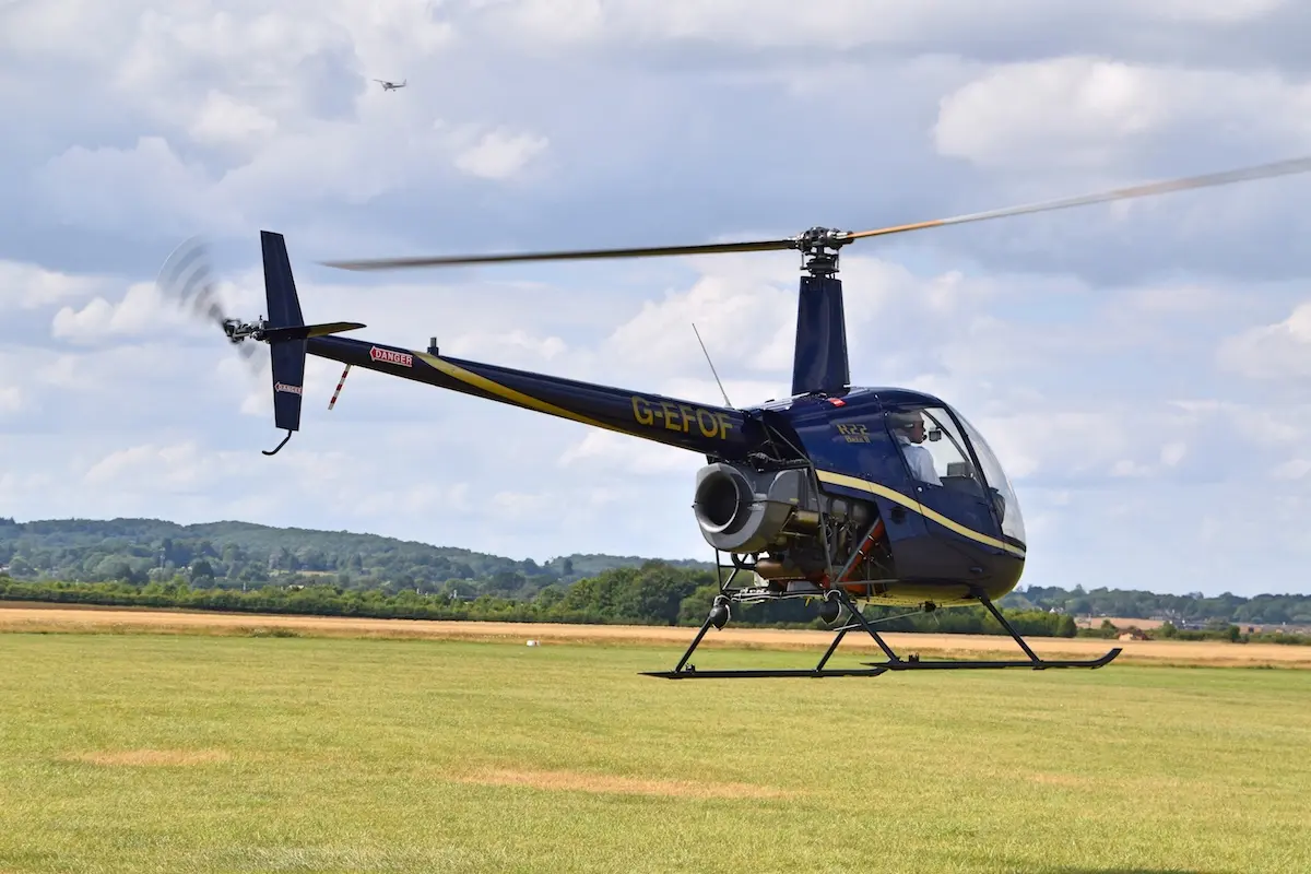 Robinson R22 training helicopter lifting off from a grass airfield